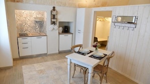 A compact kitchen with white cabinets, a tiled backsplash, and a dining table with chairs. - Vitti Suite 5 (Monopoli)