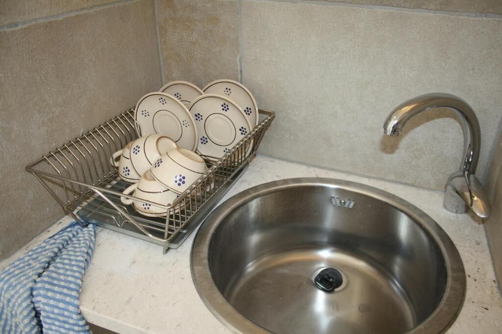 A stainless steel sink with a faucet and a dish rack holding plates and cups.