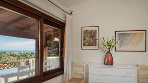 Ein Zimmer mit Balkon, einem weißen Schminktisch, zwei Stühlen und zwei gerahmten Kunstwerken an der Wand.
