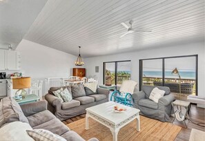 Relax in this spacious living room with a high ceiling, featuring a sofa, armchairs, and a dining area with ocean views.