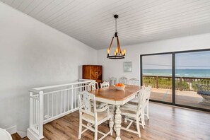 Enjoy meals in this dining area with a wooden table and comfortable chairs, overlooking the ocean from the adjacent balcony.