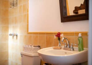 A bathroom with a white sink, a mirror, and a vase with flowers. - Casita Los Buhos (Antigua Guatemala)