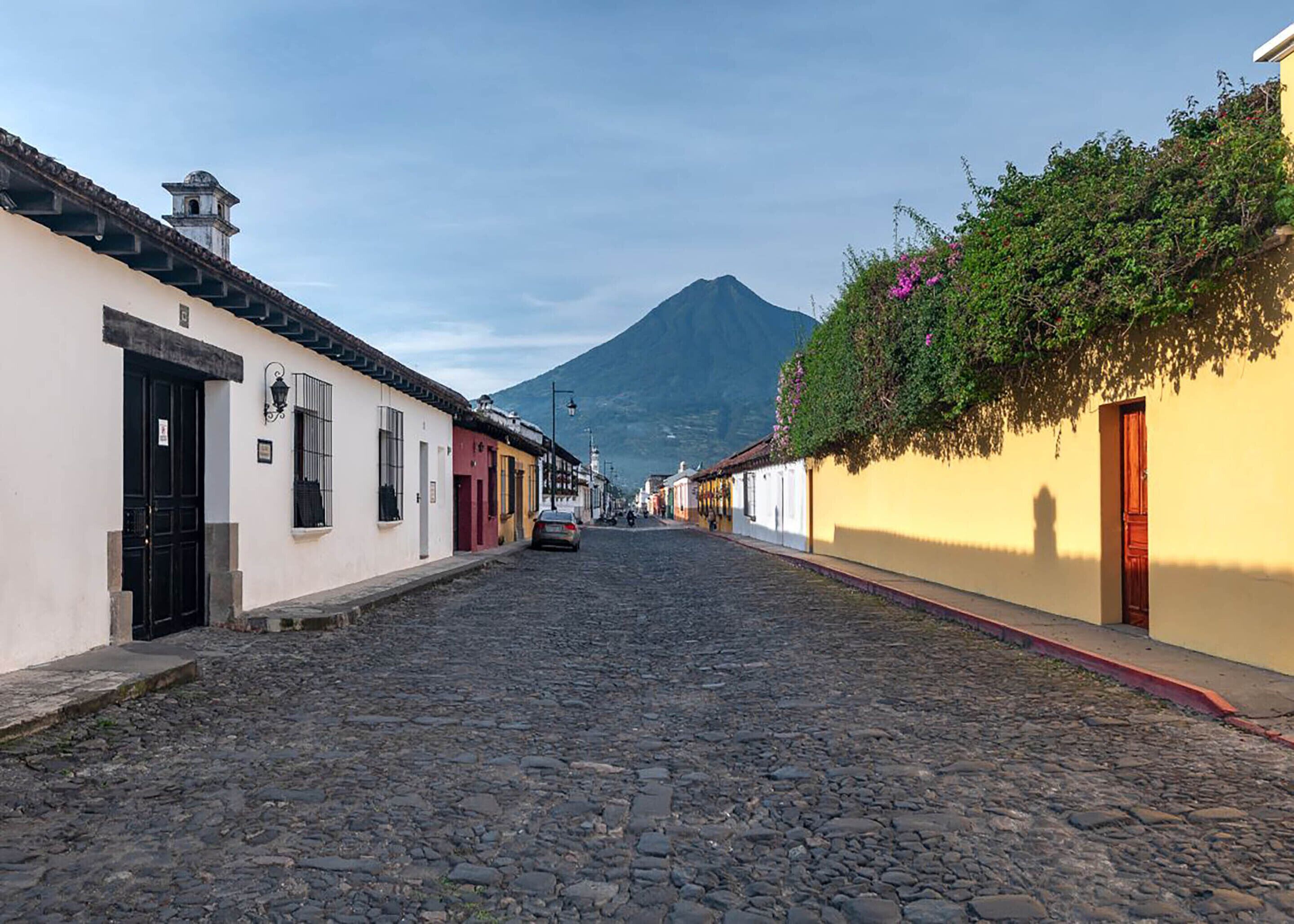 Una calle empedrada bordeada por edificios tradicionales, con una montaña al fondo y un cielo despejado.