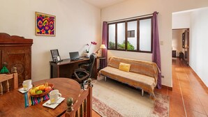A cozy room with a wooden dining table, a sofa, a desk with a laptop, and a window with curtains. - Casita Los Buhos (Antigua Guatemala)