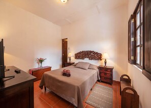 A bedroom with a bed, bedside tables, a TV, a dresser, and a window. - Casita Los Buhos (Antigua Guatemala)