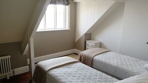 Un dormitorio con dos camas, una ventana, un radiador y una mesita de noche.