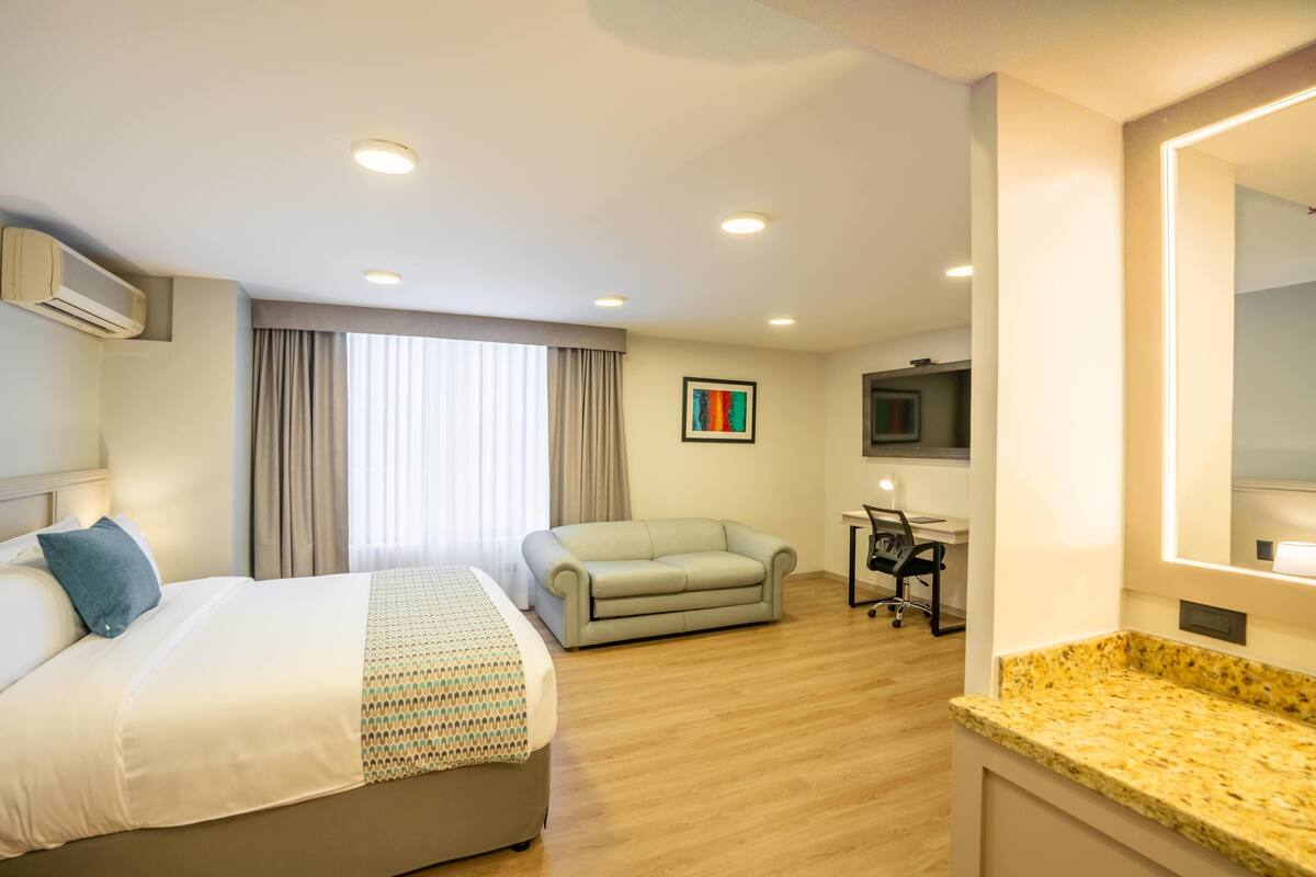 A hotel room with a bed, a sofa, a desk, and a TV.