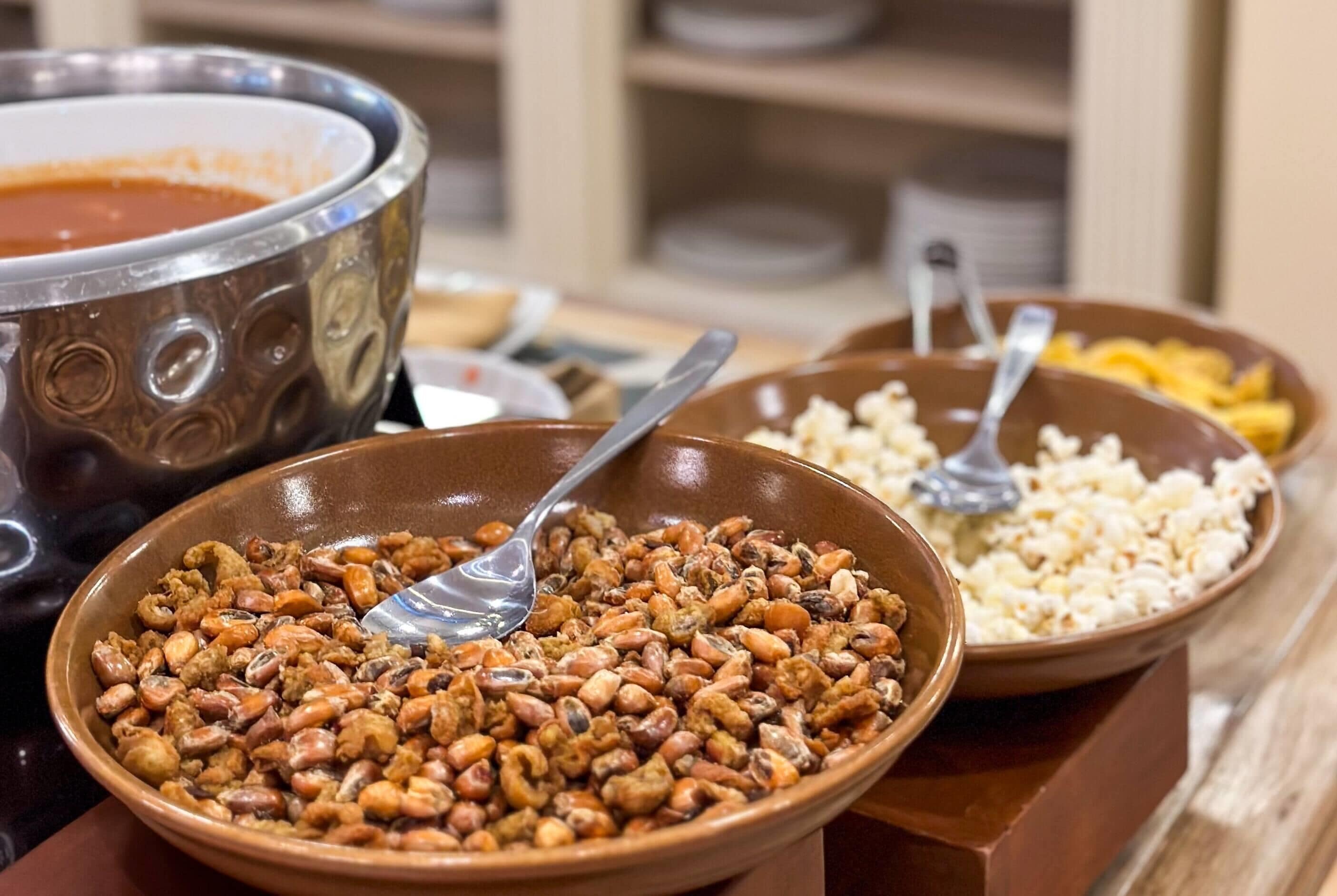 A buffet table with a variety of dishes including a large bowl of mixed nuts, a bowl of popcorn, and a bowl of soup.