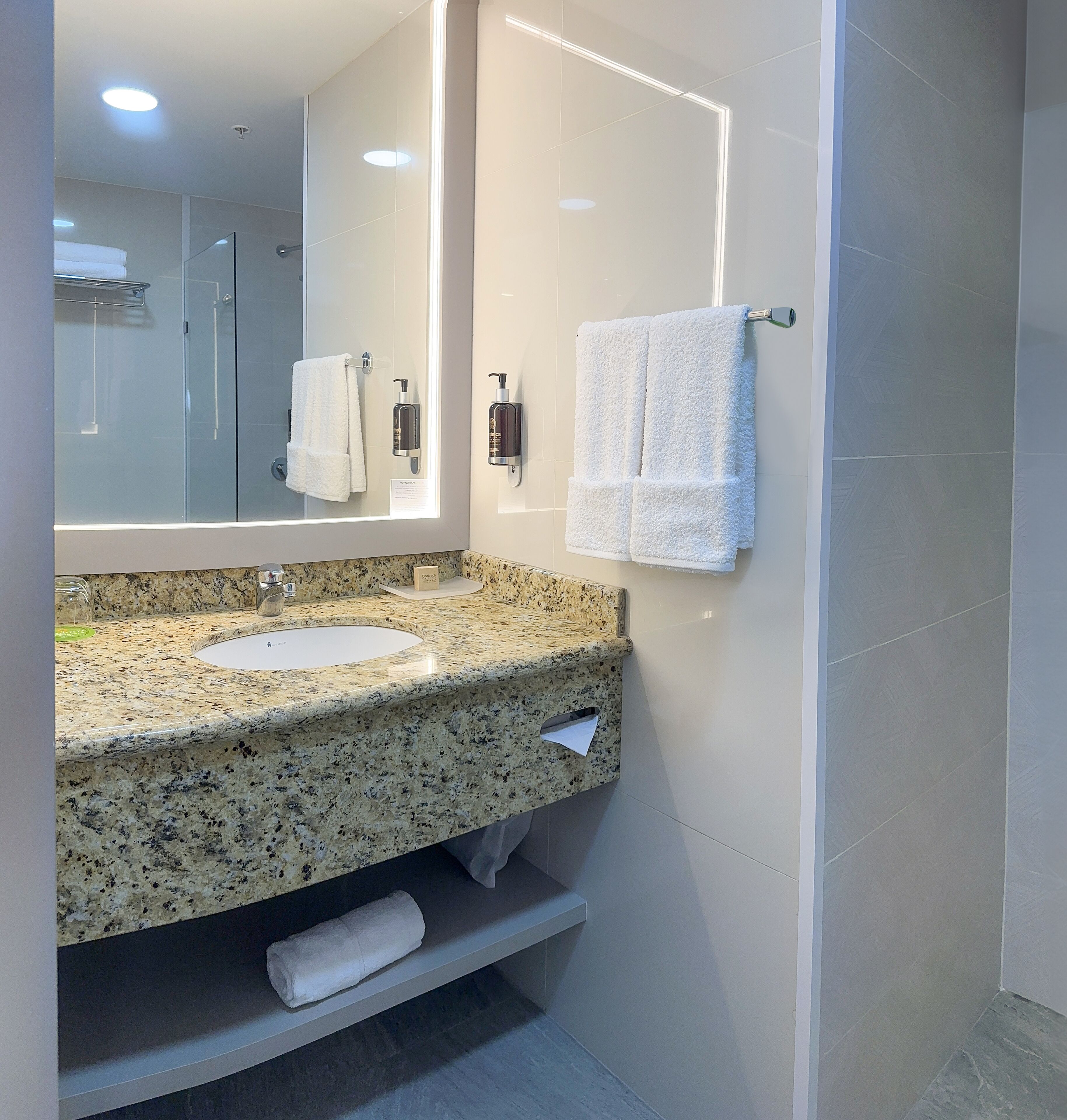 A modern bathroom with a granite countertop sink, a large mirror, and a glass shower enclosure.
