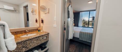 A modern bathroom with a granite countertop sink, a large mirror, and a glass shower enclosure.