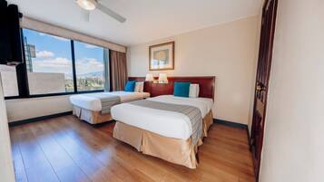 Habitación de hotel con dos camas, ventilador de techo, ventana grande con vistas y un cuadro en la pared.
