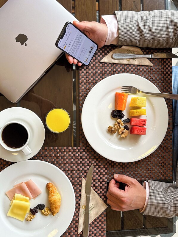 Una mesa con alimentos para el desayuno, una computadora portátil y un teléfono inteligente.