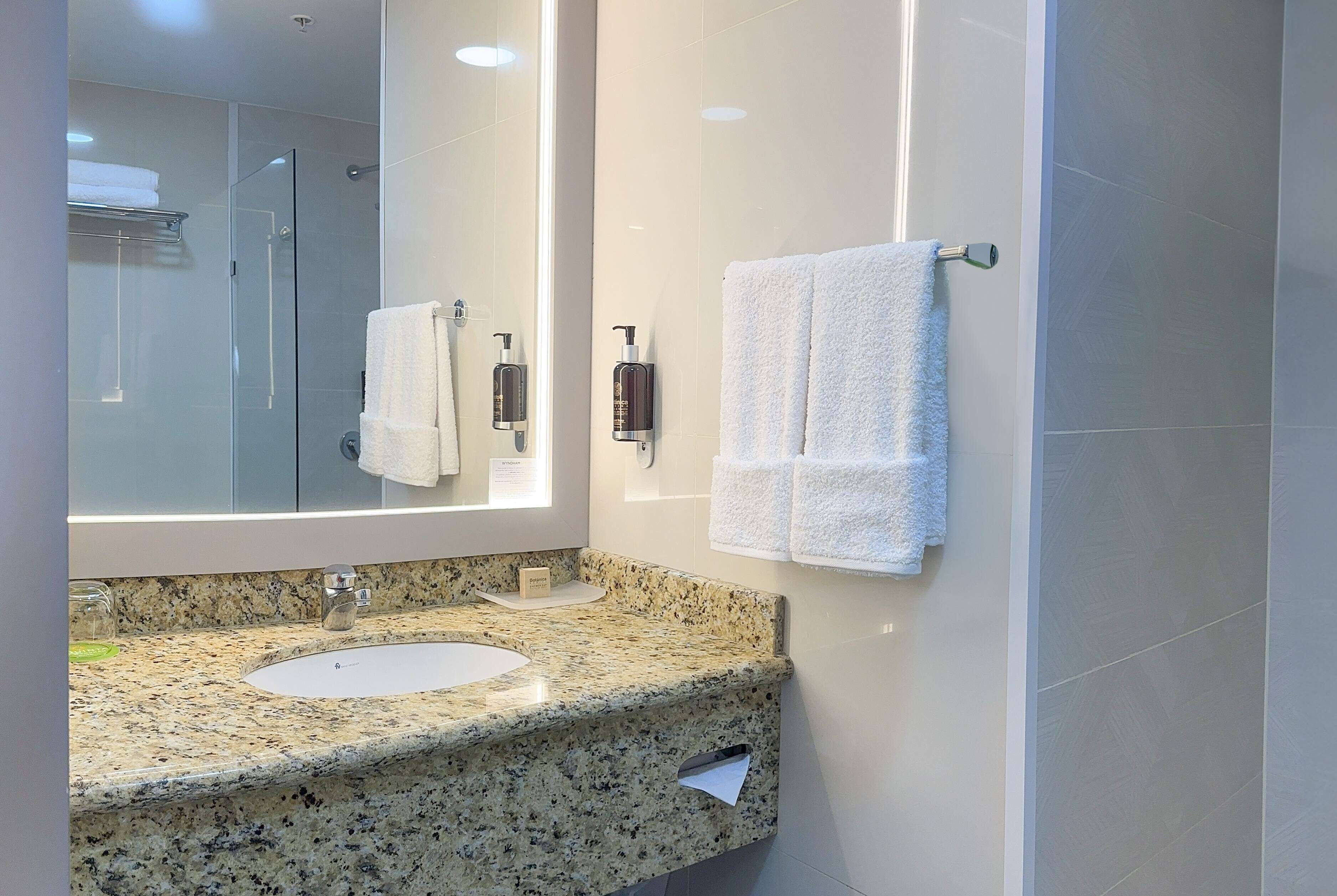 Une salle de bain moderne avec un comptoir en granit, deux vasques, un grand miroir et une cabine de douche en verre.