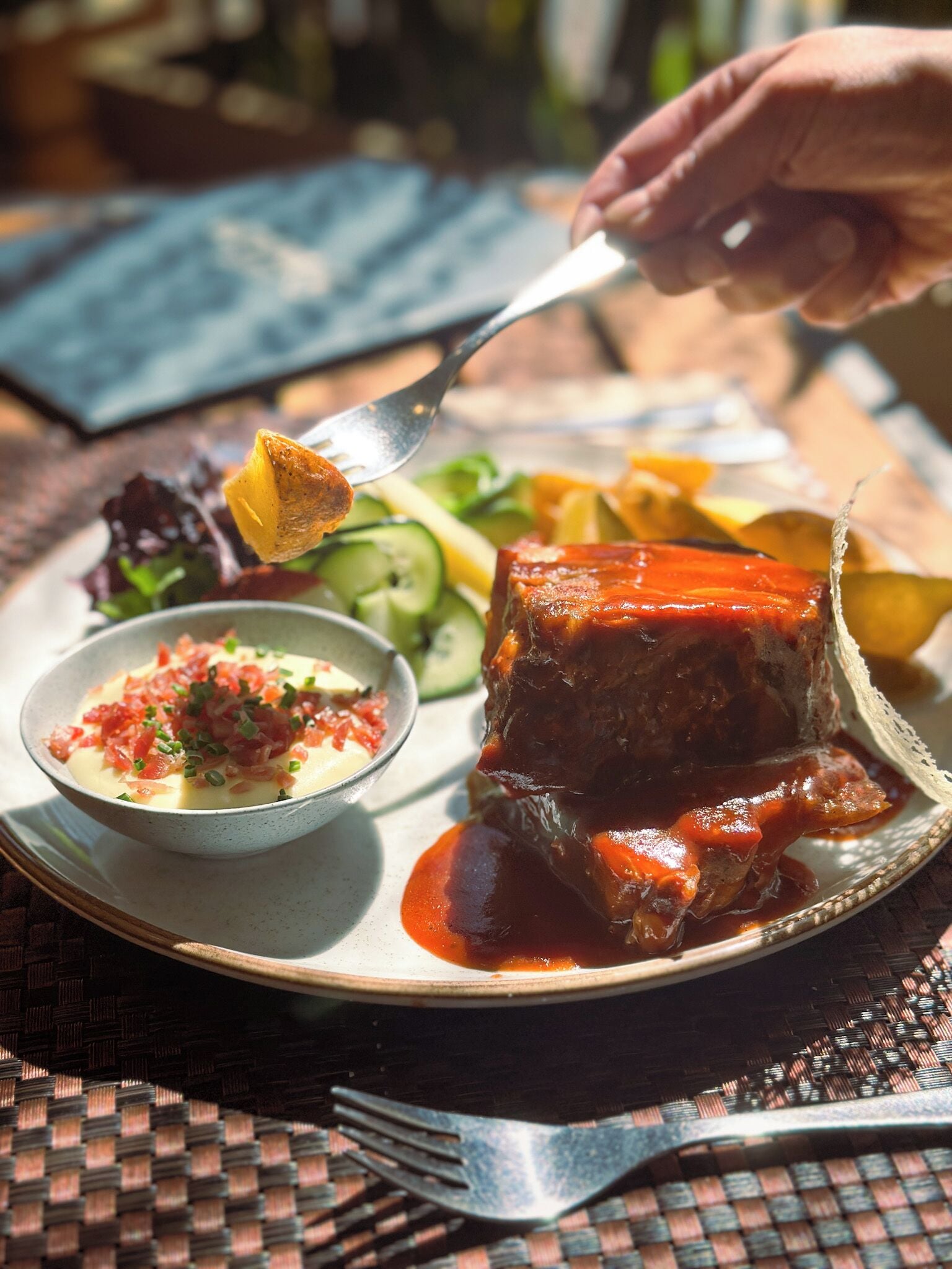 A plate with a meat dish, salad, and a small bowl of sauce.