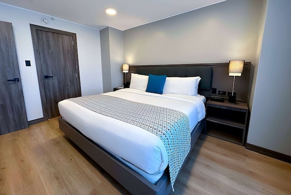 Una habitación de hotel moderna con una cama grande, suelo de madera y dos mesitas de noche con lámparas.