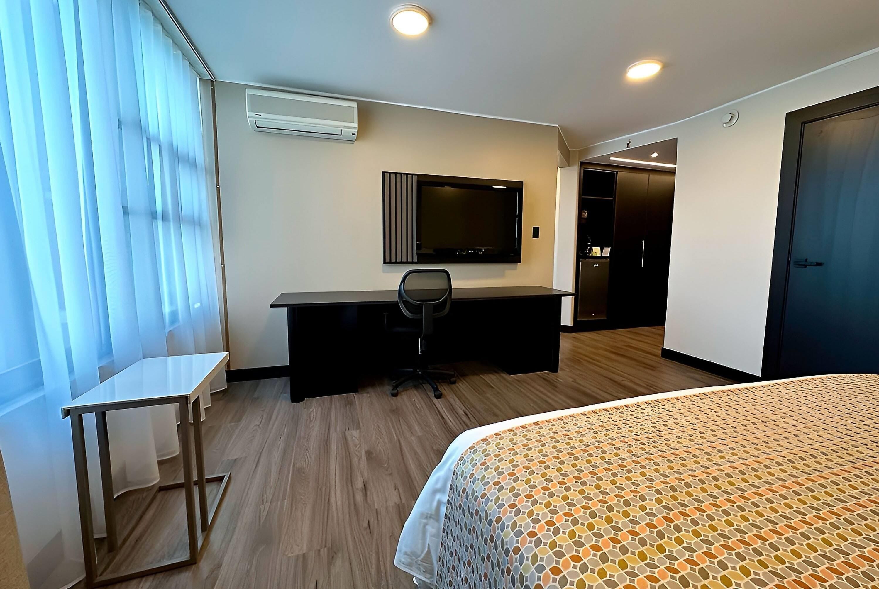 Una habitación de hotel con una cama, un escritorio, una silla, un televisor y un armario.