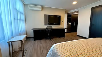 Una habitación de hotel con una cama, un escritorio, una silla, un televisor y un armario.