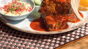 Un plato con un guiso de carne, verduras y una salsa aparte.