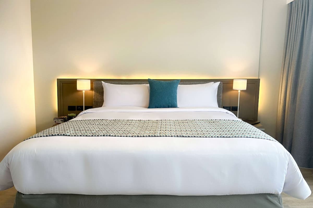 A neatly made bed with white linens and a teal accent pillow, flanked by two bedside lamps.