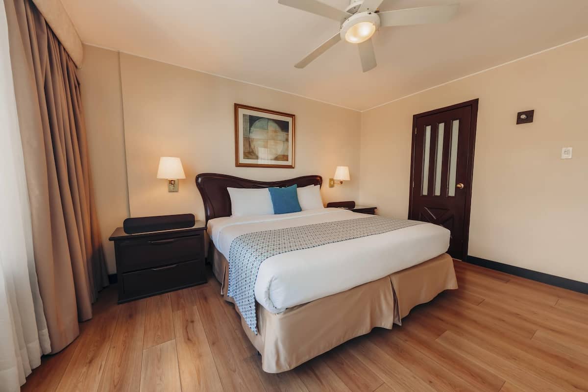 A hotel room with a bed, nightstands, a ceiling fan, and a door.