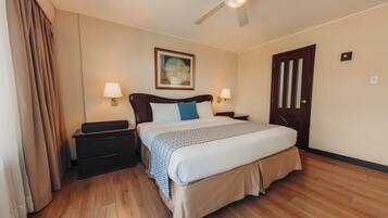 Una habitación de hotel con cama, mesitas de noche, ventilador de techo y una puerta.