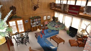 Ein geräumiges Wohnzimmer mit einem blauen Modulsofa, einem Holztisch und einem Fernseher. Ein Bücherregal voller Bücher und ein dekorativer Geweih auf der Wand sind ebenfalls zu sehen.