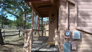 Eine rustikale Holzhütte mit überdachter Veranda, einem kleinen Tisch und einer Bank.
