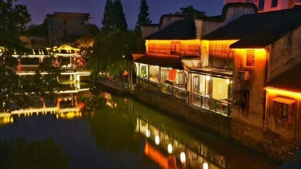 A riverside hotel with illuminated windows and a reflection in the water. - Dongfang Haomen Wangting Boutique Hotel (Huzhou)