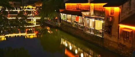A riverside hotel with illuminated windows and a reflection in the water.