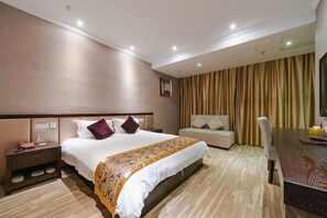 A hotel room with a large bed, a bedside table, a chair, a sofa, and a wooden table. - Dongfang Haomen Wangting Boutique Hotel (Huzhou)