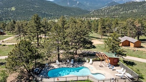 Un espace piscine doté de chaises longues et d’une terrasse en bois, entouré d’arbres et avec des montagnes en toile de fond.