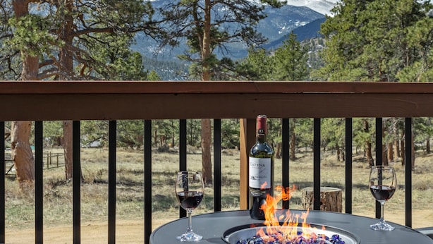 Une terrasse avec une table, deux verres de vin rouge, une bouteille de vin et un feu.