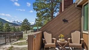Une terrasse en bois avec deux fauteuils Adirondack, une petite table sur laquelle se trouvent un saladier et des fleurs, et une clôture en bois.