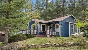 A blue house with a porch, stone wall, and surrounding trees.