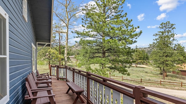 A wooden deck with benches, a railing, and a view of trees and a distant landscape.