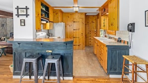 A kitchen with wooden cabinets, a central island with stools, a refrigerator, and a phone on the wall.