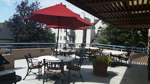 An outdoor patio area with round tables and chairs, a red umbrella, and a potted plant. - Denver/DTC Executive Corp Long/Short Term Stay Entire Condo (Greenwood Village)