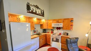 A compact kitchen with wooden cabinets, a white refrigerator, a microwave, and a stove. There is a dining area with a table and chairs.