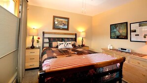A bedroom with a bed, bedside lamps, a ceiling fan, a framed picture on the wall, and a nightstand with a lamp.