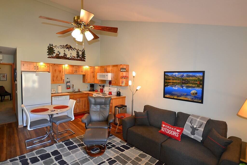 Un espacio habitable compacto con kitchenette, comedor y zona de estar con sofá y sillones.
