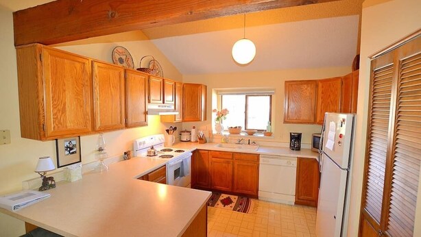 A kitchen with wooden cabinets, a central island, a sink, and a refrigerator. - Grand Estates-Spacious Two-Level Condo with Spectacular Views Near Lake Estes (Estes Park)
