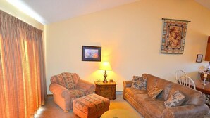 A living room with a sofa, ottoman, and a lamp on a side table. - Grand Estates-Spacious Two-Level Condo with Spectacular Views Near Lake Estes (Estes Park)