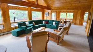 Un intérieur de chalet chaleureux avec un canapé d’angle vert, des chaises en bois et un coin repas.