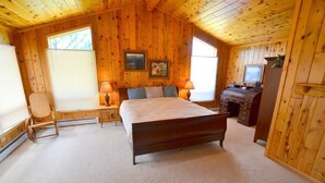 Une chambre à coucher aux murs lambrissés, avec un lit, deux tables de chevet dotées de lampes, une chaise, une commode et un téléviseur.