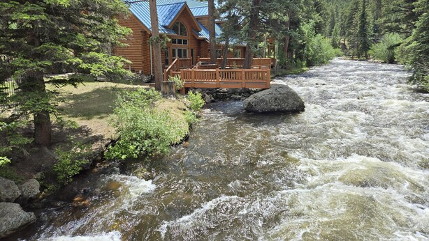 A log cabin with a blue roof, situated by a fast-flowing river, surrounded by dense forest.