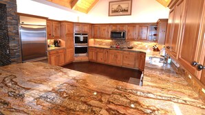 A spacious kitchen with granite countertops, wooden cabinets, stainless steel appliances, and a stone fireplace.