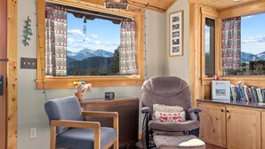 Ein gemütliches Zimmer mit Bergblick, Holzboden, einem Schreibtisch mit Stuhl und einem Fenster mit gemusterten Vorhängen.