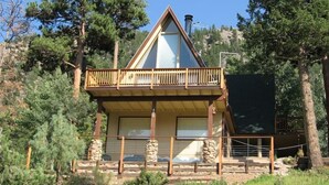 A cabin with a wooden balcony, stone pillars, and a clear view of the surrounding forest. - Peak View - 4 bedroom A-frame with great views (Estes Park)
