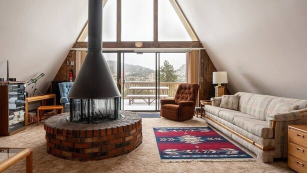 A cozy loft bedroom with a large chimney, a view of the outdoors, a comfortable sofa, and a wooden desk. - Peak View - 4 bedroom A-frame with great views (Estes Park)