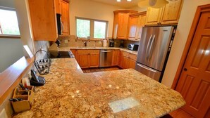 Una cocina con encimeras de granito, gabinetes de madera y electrodomésticos de acero inoxidable, con un ventanal que aporta luz natural.